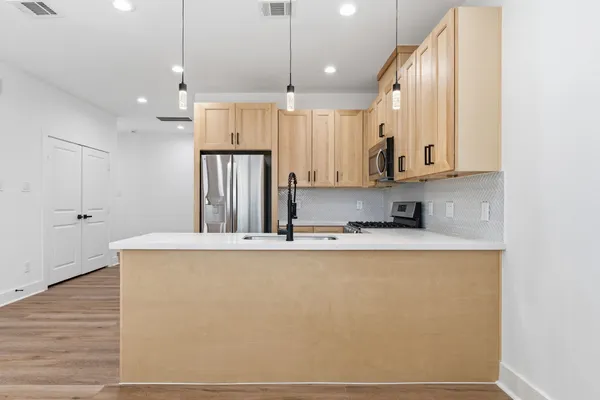 a large kitchen with kitchen island a stove a sink a refrigerator and white cabinets with wooden floor