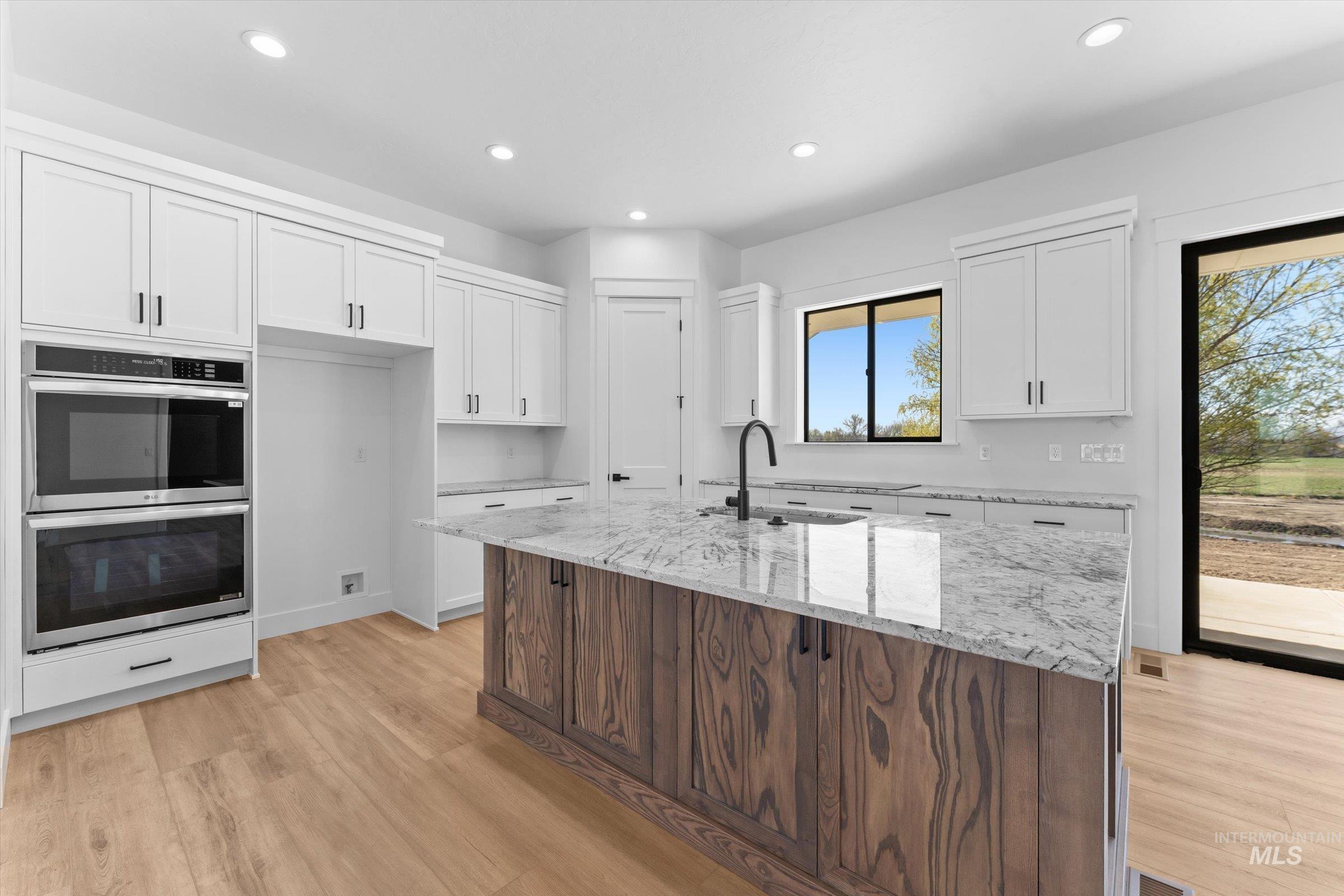 26219 Reed Lane Wilder, ID 83676 - Photo 7 of 35 Two tone kitchen with light stone countertops, double oven, a center island with sink, light wood-style floors, and recessed lighting
