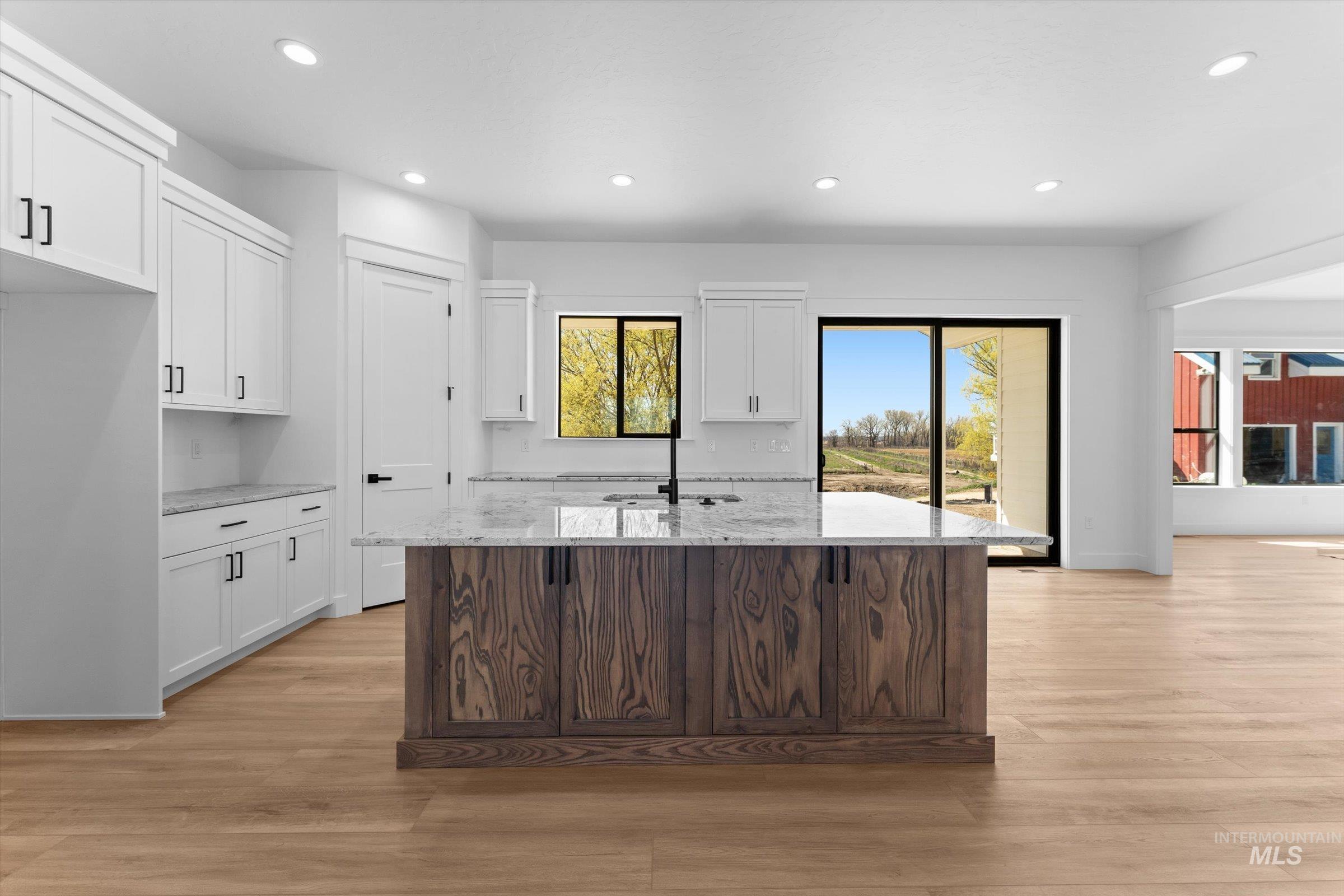 26219 Reed Lane Wilder, ID 83676 - Photo 8 of 35 Two tone kitchen with light stone counters, light wood-type flooring, recessed lighting, a center island with sink, and two tone cabinetry