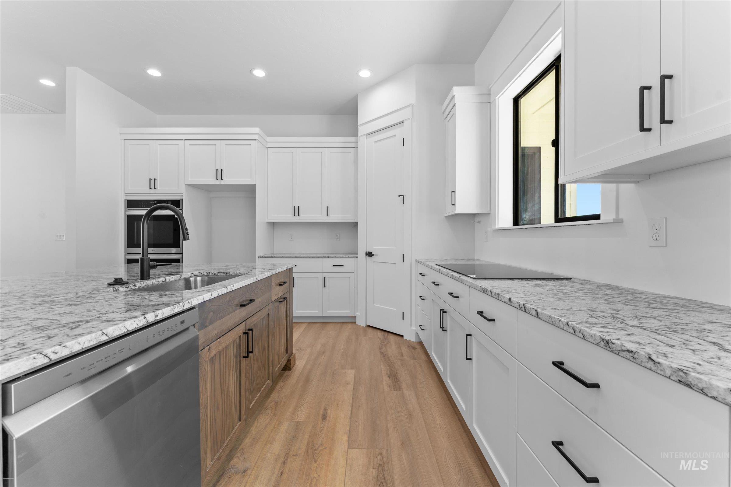 26219 Reed Lane Wilder, ID 83676 - Photo 9 of 35 Two tone kitchen with two tone cabinetry, stainless steel appliances, light stone counters, light wood-style floors, and recessed lighting