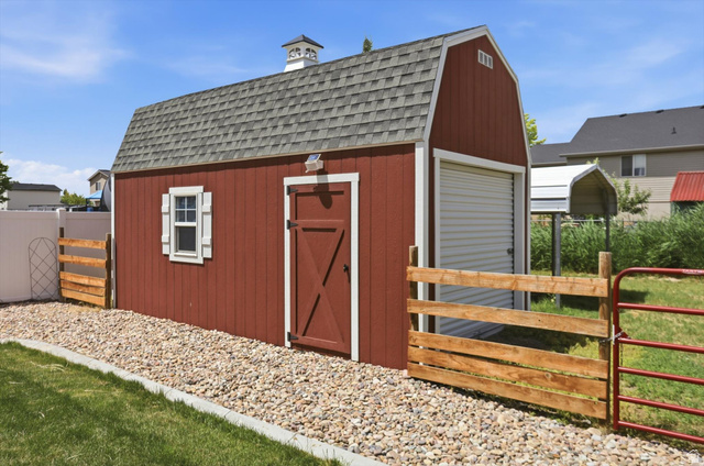 3636 West 910 South Syracuse, UT 84075 - Photo 67 of 70 Red barn-style shed featuring a gray shingle roof, cupola, white window with shutters, and a roll-up garage door