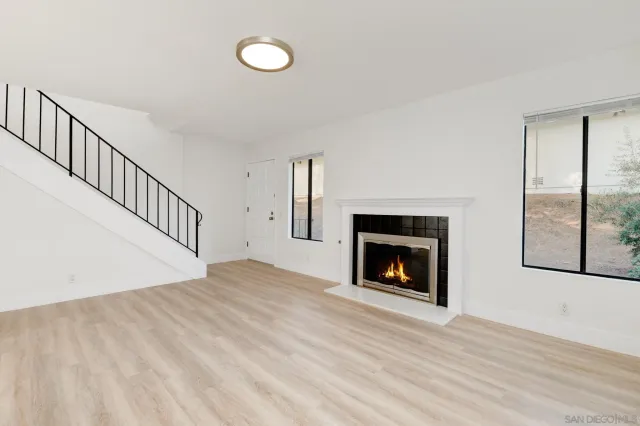 a view of an empty room with wooden floor fireplace and a window