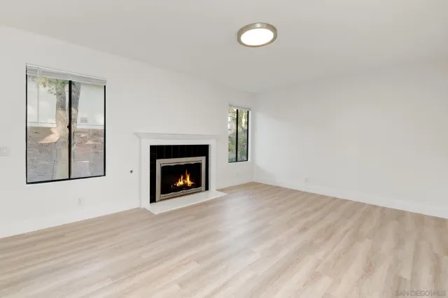 a view of an empty room with wooden floor fireplace and a window