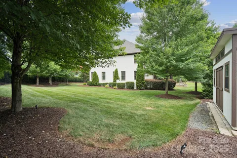 a view of a white house in front of a big yard with large trees