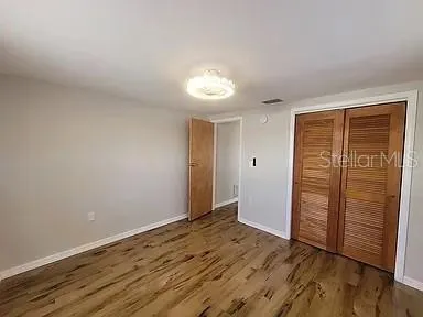 a view of an empty room with wooden floor and closet