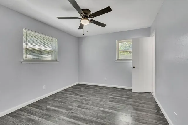 an empty room with wooden floor ceiling fan and windows