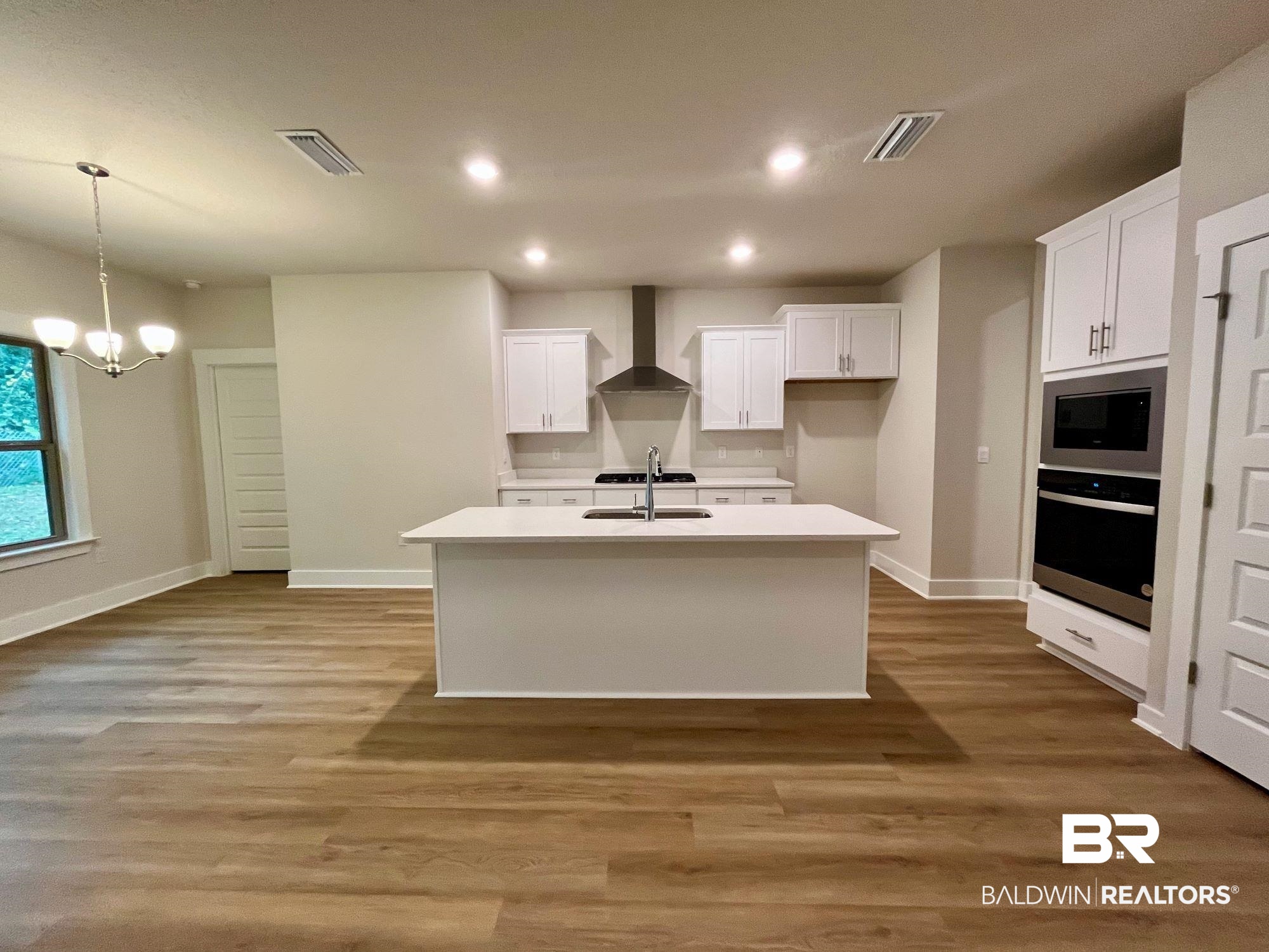 330 Barndling Street Fairhope, AL 36532 - Photo 11 of 31 Kitchen featuring white cabinetry, appliances with stainless steel finishes, an island with sink, wall chimney exhaust hood, and light hardwood / wood-style flooring