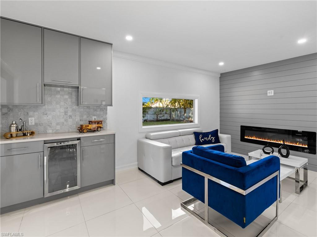 1837 51st Terrace Southwest Naples, FL 34116 - Photo 14 of 35 Bar area featuring: picture window, wine fridge, high gloss cabinets, quartz countertop, crown molding, shiplap accent wall, recessed lighting, and a electric heated fireplace.
