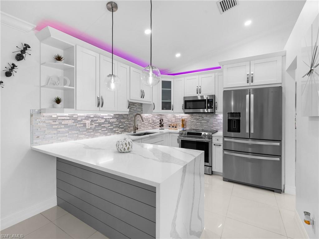 1837 51st Terrace Southwest Naples, FL 34116 - Photo 6 of 35 Kitchen with stainless steel appliances, quartz countertop, Vaulted ceiling, decorative backsplash, light tile patterned floors, and white cabinets