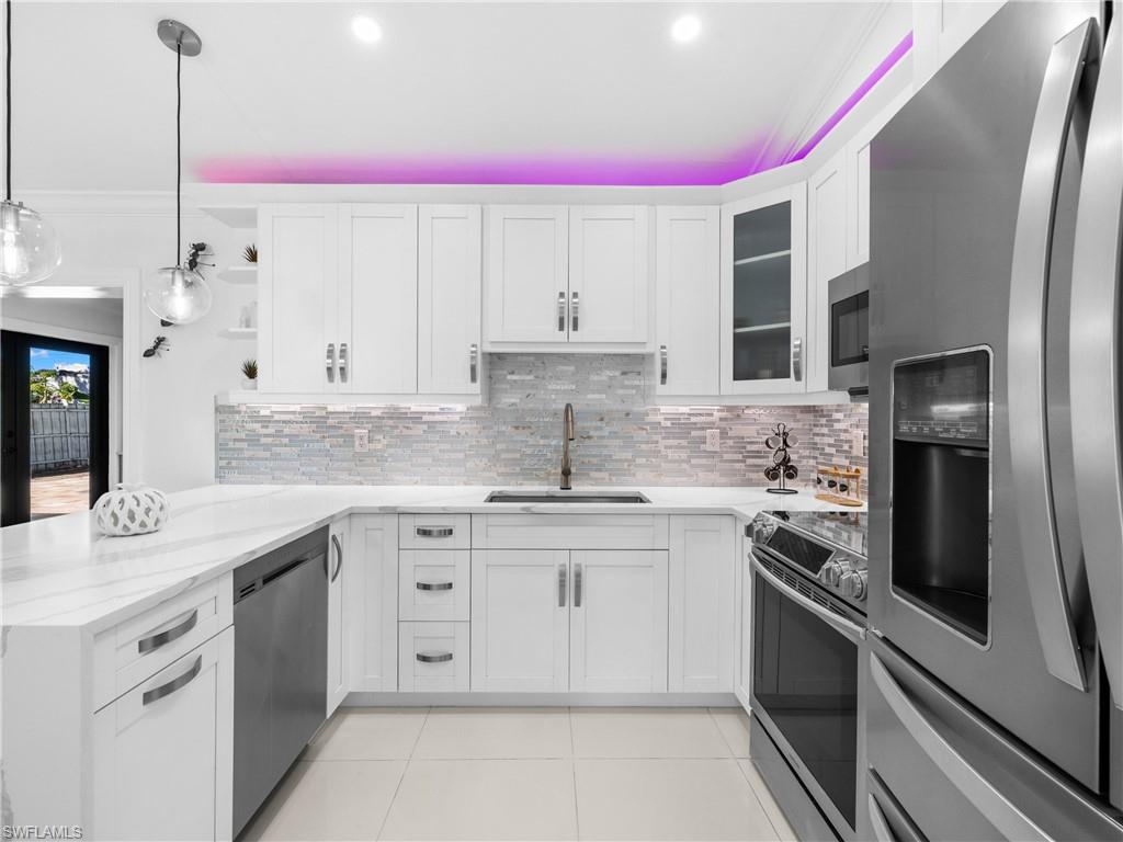 1837 51st Terrace Southwest Naples, FL 34116 - Photo 7 of 35 Kitchen with appliances with stainless steel finishes, quartz countertop, tasteful backsplash, a peninsula, open shelves, and white cabinetry
