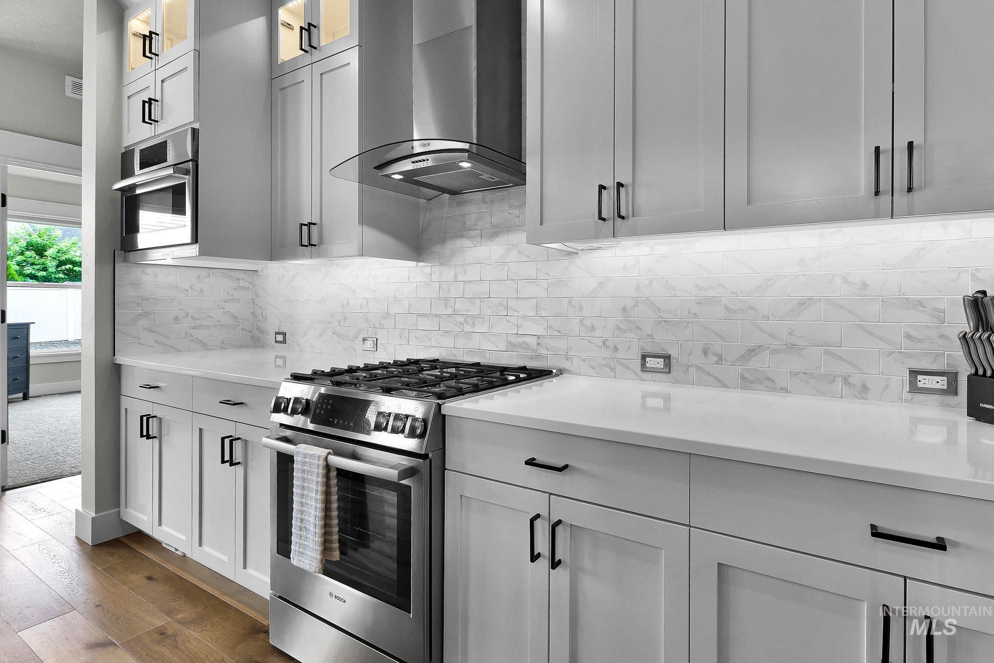 5676 East Zaffre Ridge Street Boise, ID 83716 - Photo 13 of 50 Modern kitchen featuring light gray cabinetry, stainless steel appliances, a gas range with a coordinating range hood, white countertops, and a white subway tile backsplash