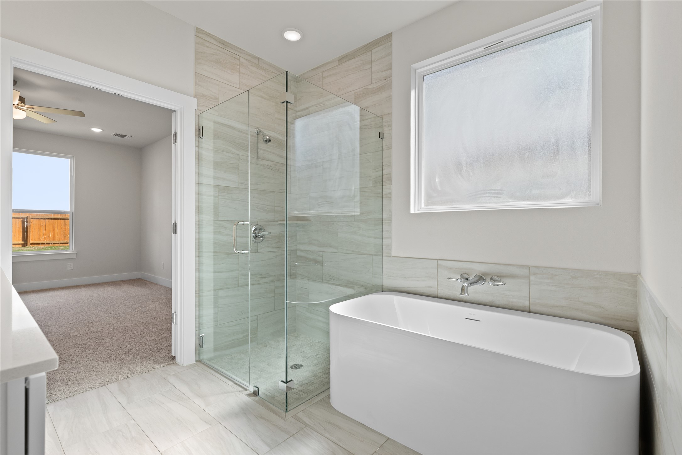 19705 Domino Champ Road Pflugerville, TX 78660 - Photo 26 of 38 A modern soaking tub stands alongside a glass-enclosed walk-in shower with tiled walls.