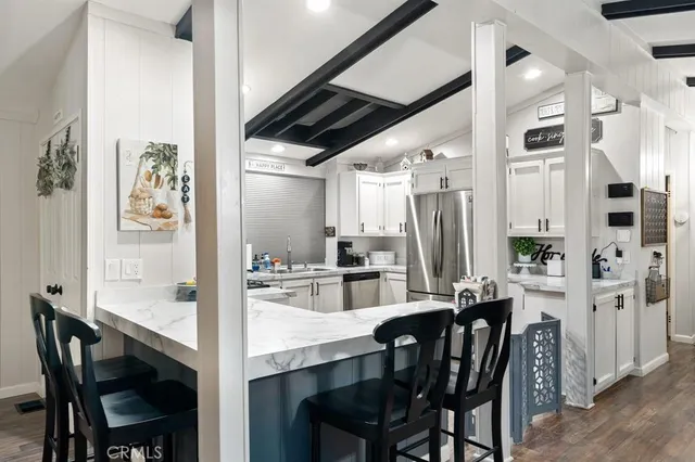 a kitchen with stainless steel appliances kitchen island granite countertop a dining table chairs and a refrigerator