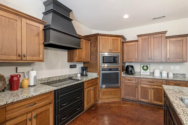 a kitchen with stainless steel appliances granite countertop a stove top oven a sink dishwasher and a refrigerator with wooden cabinets