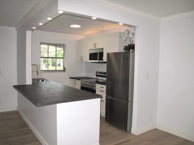 a kitchen with stainless steel appliances granite countertop a refrigerator a sink a stove and a refrigerator with wooden floor