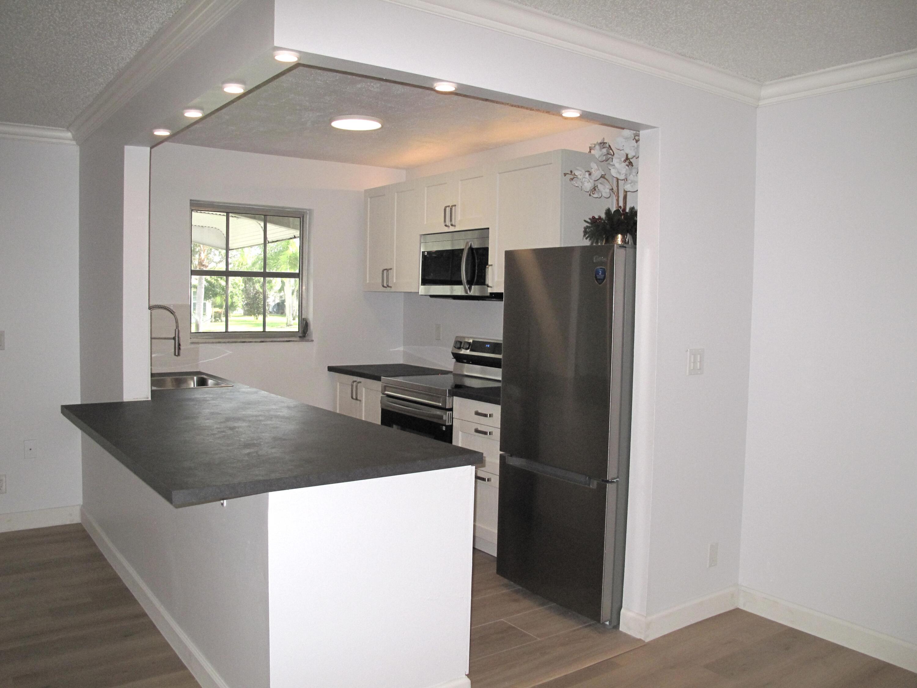 1102 North Drive, Unit C Delray Beach, FL 33445 - Photo 7 of 36 a kitchen with stainless steel appliances granite countertop a refrigerator a sink a stove and a refrigerator with wooden floor