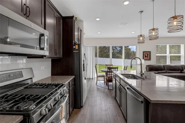 a kitchen with granite countertop a stove a sink a refrigerator wooden floor and cabinets