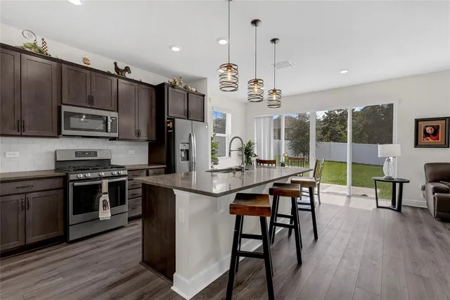 a kitchen with stainless steel appliances granite countertop a stove a sink a refrigerator and a dining table with wooden floor