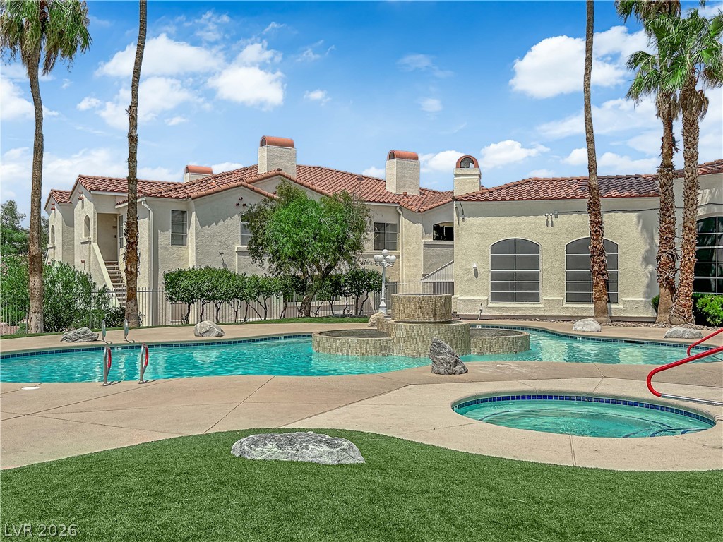 698 South Racetrack Road, Unit 1521 Henderson, NV 89015 - Photo 32 of 33 A refreshing pool and spa area with a fountain, set against a Mediterranean-style building under a bright sky.