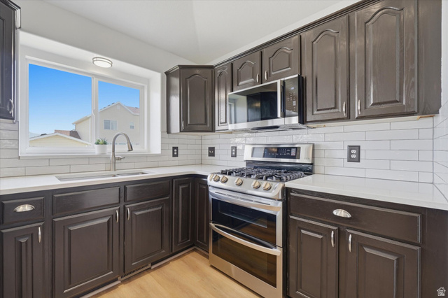 5576 South 4100th Street West Roy, UT 84067 - Photo 8 of 35 Contemporary kitchen featuring dark cabinetry, white countertops, stainless steel appliances, and a subway tile backsplash