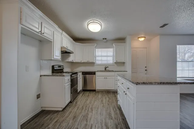 a kitchen with granite countertop a stove top oven a sink dishwasher and a fireplace with wooden floor