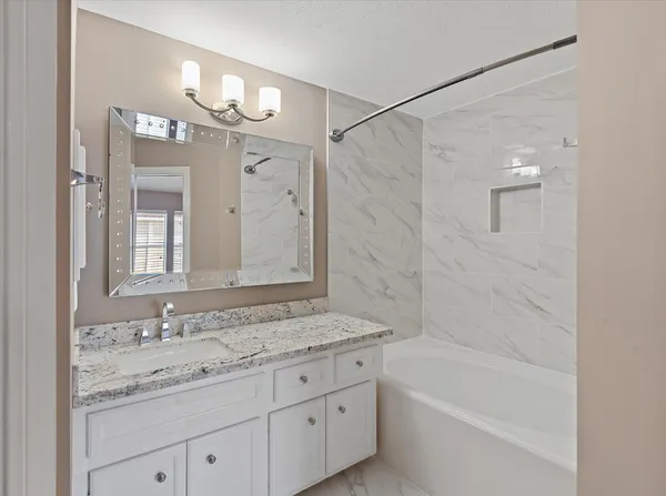 a bathroom with a granite countertop sink a mirror a bathtub and shower
