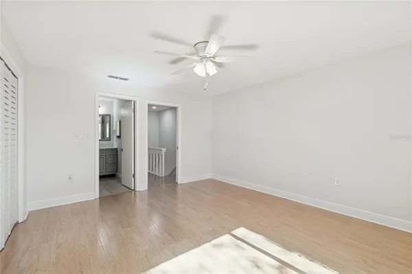 an empty room with wooden floor chandelier fan and windows