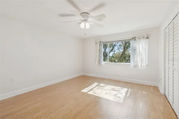 a view of an empty room with wooden floor and a ceiling fan
