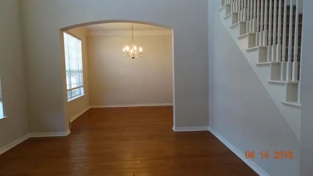 an empty room with wooden floor staircase and windows