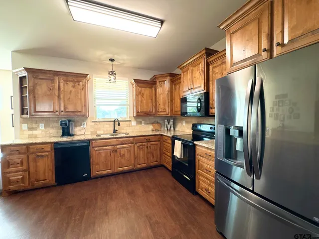 a kitchen with stainless steel appliances granite countertop a refrigerator a sink dishwasher a stove and white countertops with wooden floor