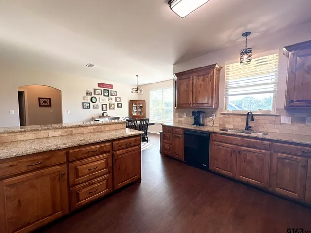 a kitchen with stainless steel appliances granite countertop wooden floors wooden cabinets a sink and a window