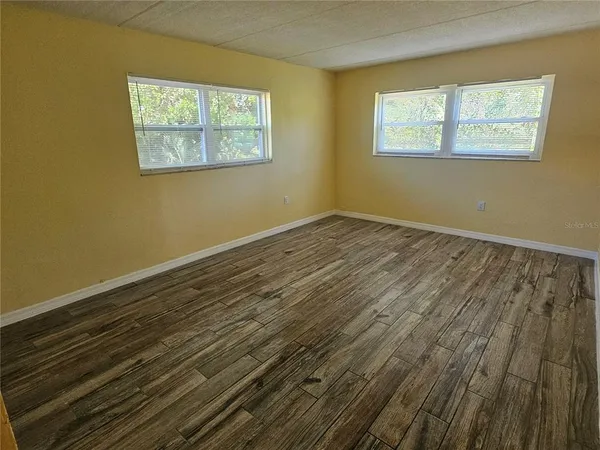 a view of an empty room with wooden floor and a window