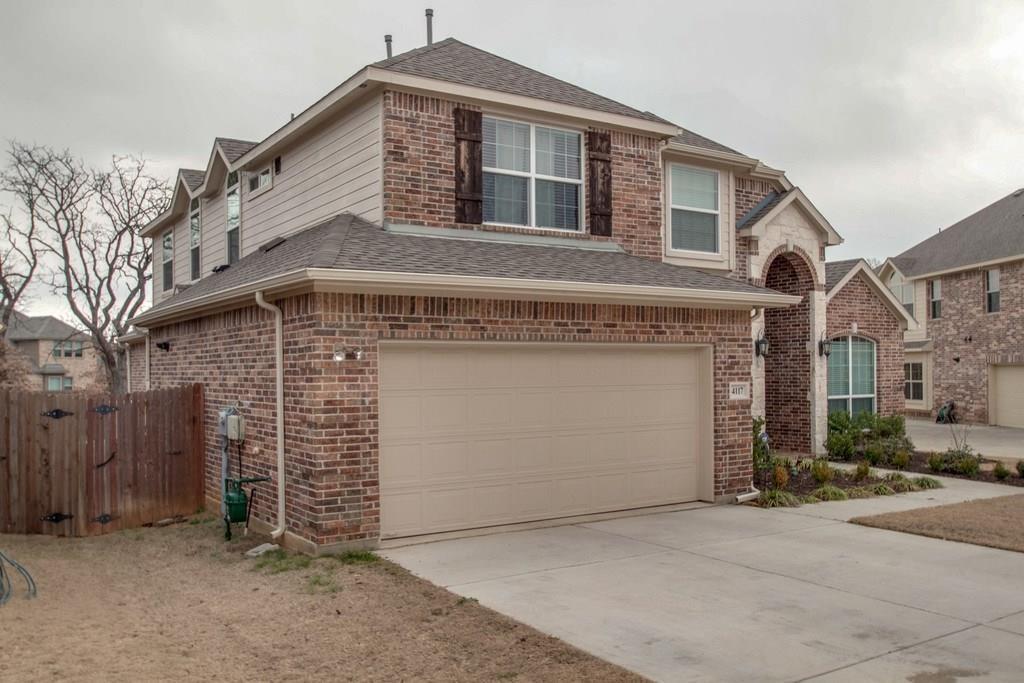 4117 Autumn Path Road Denton, TX 76208 - Photo 4 of 4 Two-story residence featuring a brick and siding exterior, an arched entryway with stone detailing, an attached two-car garage, multiple windows with dark shutters, and a sloped roofline