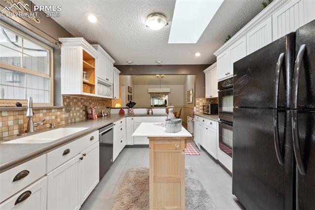 7475 Chirgiton Road Colorado Springs, CO 80908 - Photo 14 of 38 Kitchen featuring black appliances, a sink, a skylight, backsplash, and a kitchen island