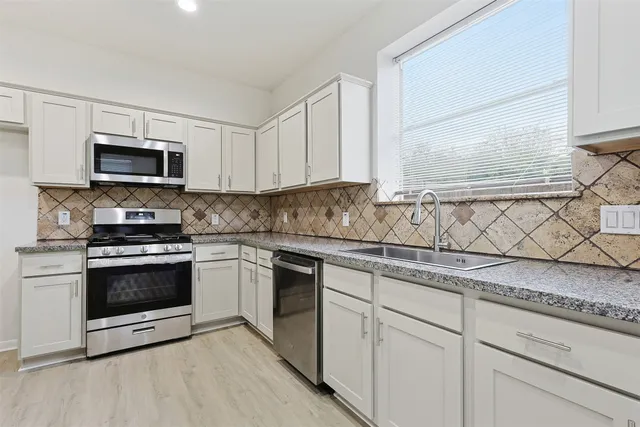 a kitchen with white cabinets a sink and a stove with wooden floor