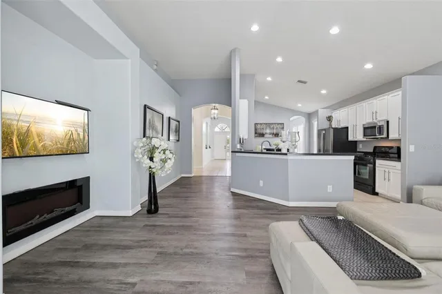 a living room with stainless steel appliances furniture wooden floor and a kitchen view