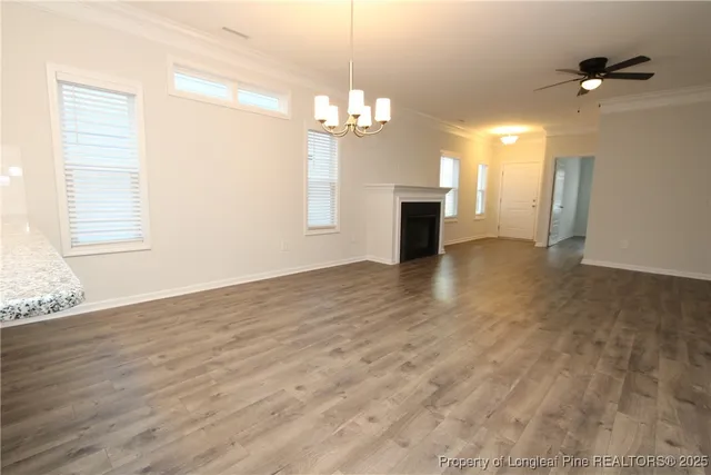 an empty room with wooden floor chandelier fan and windows
