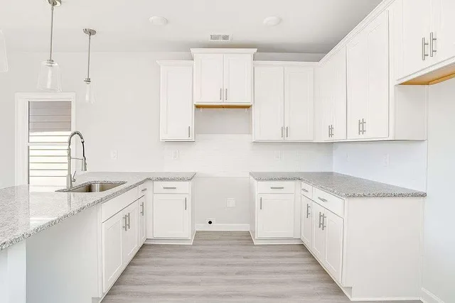 a large white kitchen with granite countertop a stove a sink and dishwasher with white cabinets