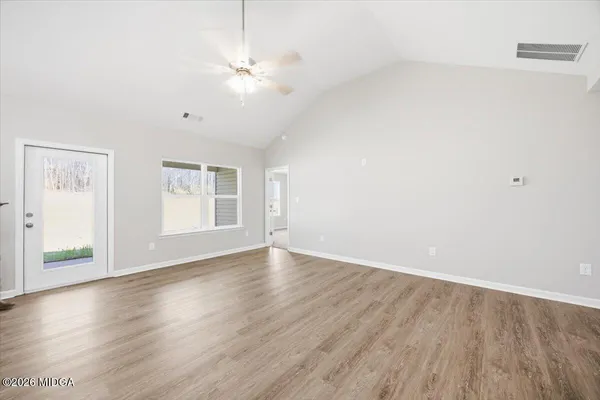 an empty room with wooden floor chandelier fan and windows