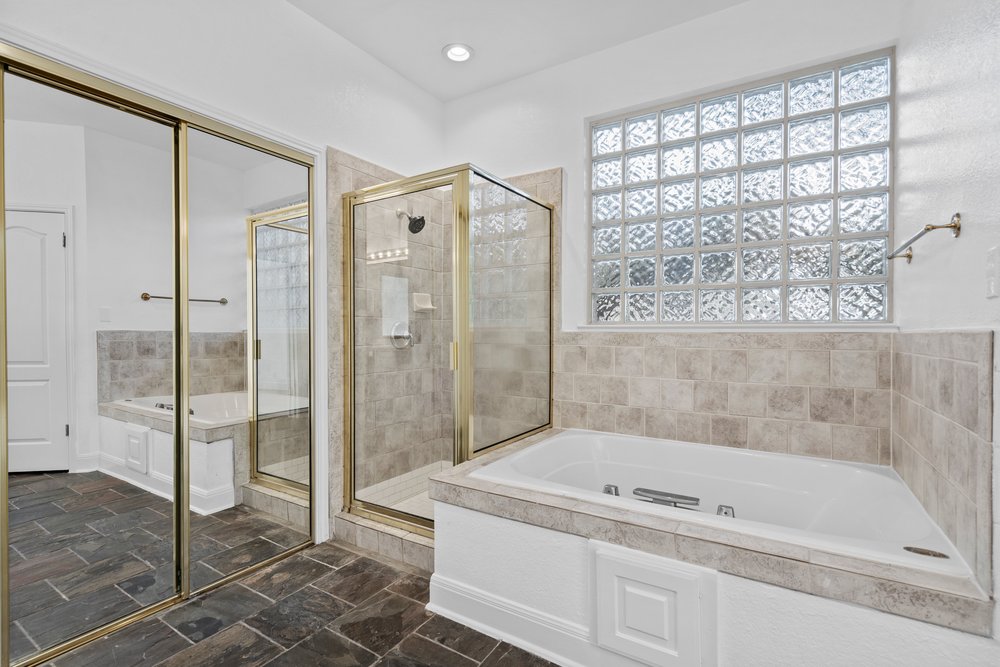 1815 Rue De St Tropez Austin, TX 78746 - Photo 33 of 40 Spacious bathroom featuring a built-in soaking tub, glass block window, and a separate glass-enclosed shower with gold-tone hardware