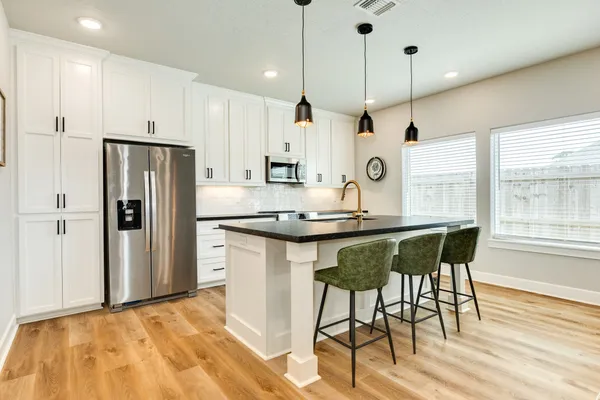 a kitchen with stainless steel appliances granite countertop a stove a sink a microwave a refrigerator and white cabinets with wooden floor