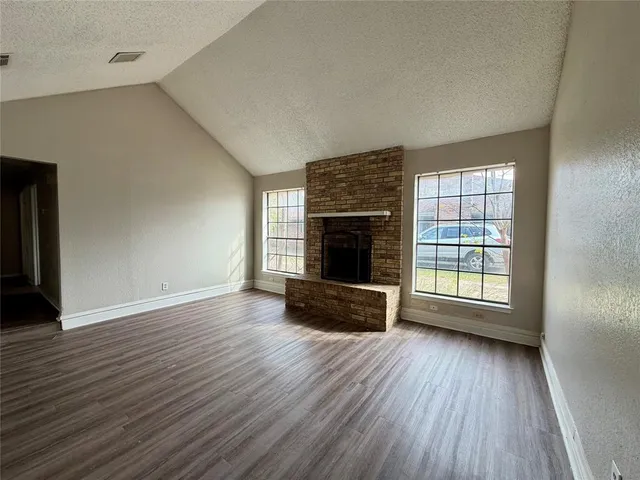 an empty room with wooden floor fireplace and windows
