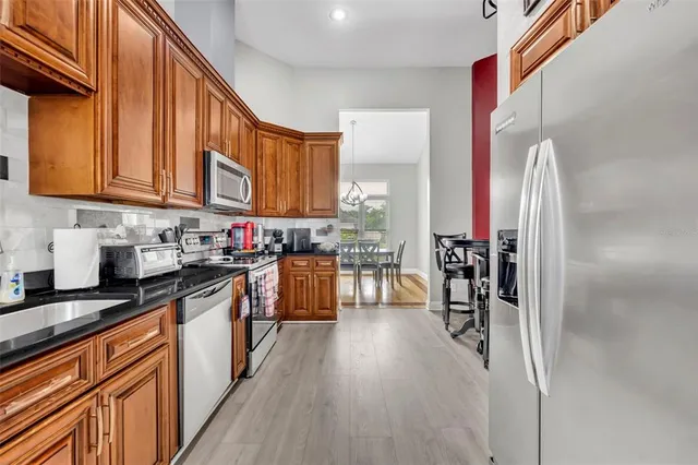 a kitchen with stainless steel appliances granite countertop a refrigerator a sink dishwasher a stove and white cabinets with wooden floor