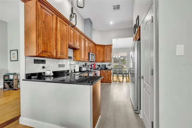 a kitchen with stainless steel appliances granite countertop a refrigerator a sink dishwasher a stove and a dining table with wooden floor