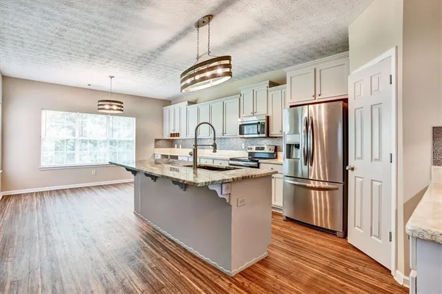 a kitchen with stainless steel appliances granite countertop a refrigerator a sink dishwasher a stove and white countertops with wooden floor