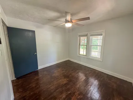 an empty room with wooden floor fan and windows