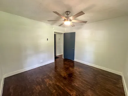 an empty room with wooden floor chandelier fan and windows
