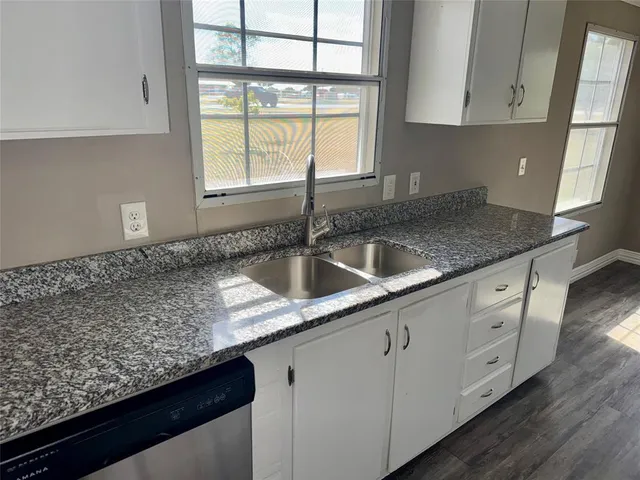 a kitchen with granite countertop stainless steel appliances a sink window and cabinets