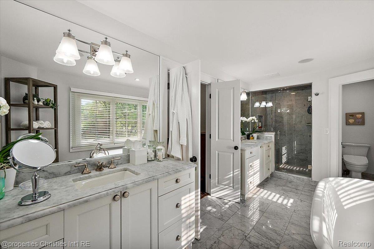 528 Covington Road Bloomfield Hills, MI 48301 - Photo 32 of 75 Bathroom featuring a double vanity with stone countertops, a large glass-enclosed shower, a separate soaking tub, and stone tile flooring