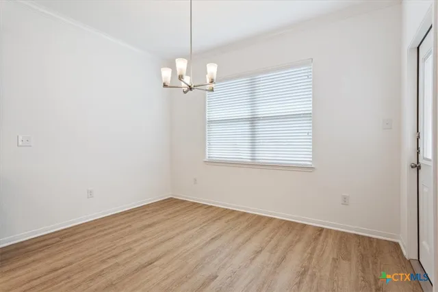 an empty room with wooden floor a chandelier and windows